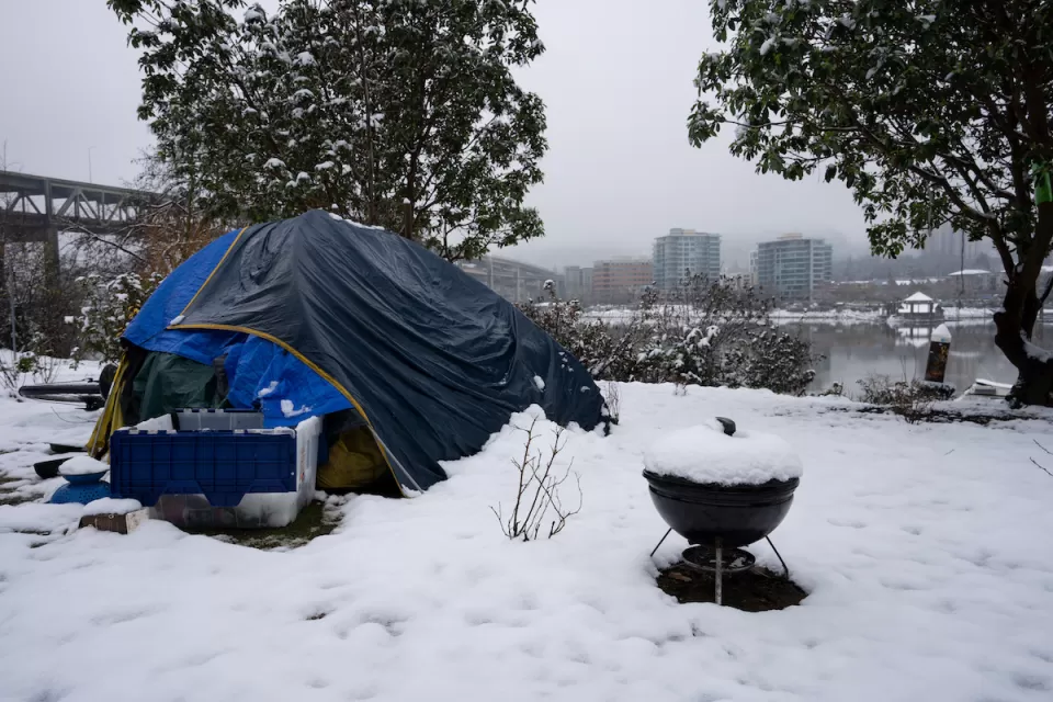 Blue tent with small charcoal grill and plastic bin set up by unhoused person in snow in Portland, Oregon.